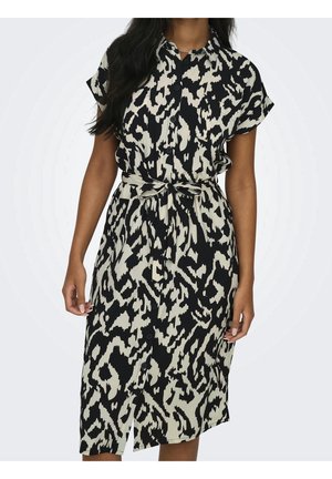 Femme portant une robe-chemise à boutonner, à motif abstrait noir et blanc, avec manches courtes et ceinture nouée à la taille.