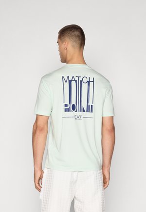 Tricou scurt cu mâneci scurte, de culoare verde mentă deschisă, cu un grafic îndrăzneț „MATCH POINT” în nuanță de navy pe spate. Material neted și croială lejeră.