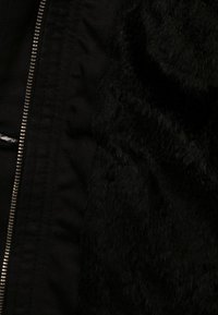 Giacca nera con una combinazione di tessuto liscio e morbida pelliccia testurizzata. Chiusura a zip evidenziata lungo la cucitura. Nessun motivo o accento visibile.