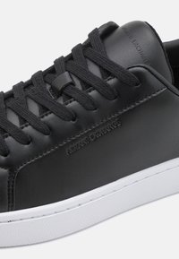 Schwarze Ledersneaker mit flachen schwarzen Schnürsenkeln, geprägtem Logo an der Seite, glatter Oberfläche und weißer Gummisohle mit strukturiertem Grip.
