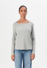 Gray long-sleeve top with a scoop neckline. Made of a soft, textured fabric with a slightly curved hem. Paired with blue denim jeans.