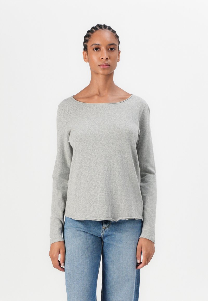 Gray long-sleeve top with a scoop neckline. Made of a soft, textured fabric with a slightly curved hem. Paired with blue denim jeans.