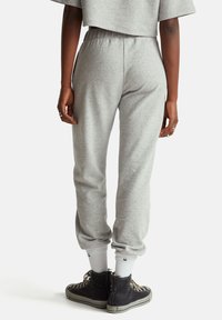 Šedé tepláky sličně zúženého střihu a elastickým pasem, doplněné černými kotníkovými botami a bílými vysokými ponožkami.