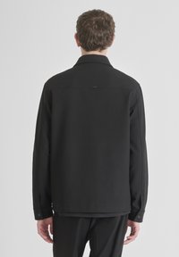 Giacca nera con un design strutturato, maniche lunghe e chiusura a bottone sui polsini. Tessuto liscio con un minimo dettaglio del logo sul retro.