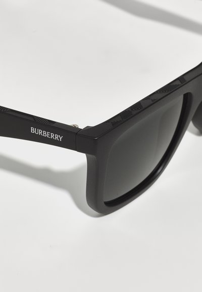 Ochelari de soare dreptunghiulari negri cu un cadru texturat, prezentând o finisare mată. Lentilele sunt întunecate și ușor reflectorizante. Branding Burberry pe lateral.
