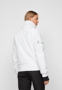 Weiße isolierte Jacke mit hohem Kragen, elastischen Bündchen und einer Seitentasche. Glatte Textur, taillierter Schnitt, geeignet für kaltes Wetter.