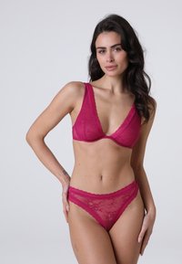 Reggiseno in pizzo e perizoma abbinato di un rosa intenso. Il reggiseno presenta un scollatura profonda e spalline larghe. Entrambi gli articoli hanno bordi ondulati e motivi floreali.