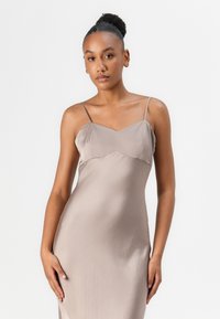 Abito slip in seta di un tenue color taupe, con un corpetto aderente e scollo a V, spalline sottili e regolabili, texture liscia e lunghezza fino al pavimento.