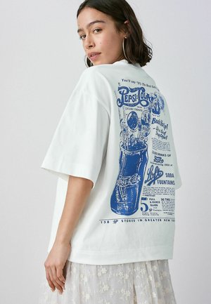 Biele oversized tričko s modrou grafickou potlačou fľaše Pepsi a retro nápisom na chrbte. Krátke rukávy a mäkká tkanina.