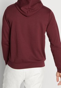 Sudadera burdeos con un corte relajado, que presenta una capucha con cordón, puños acanalados y una cinturilla acanalada, fabricada con una suave tela texturizada.