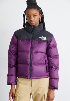 Chaqueta acolchada morada con acentos negros, cuello alto, cremallera frontal y bolsillos laterales. Presenta un texturizado acolchado y un logo en el lado izquierdo del pecho.