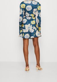 Robe portefeuille à motifs floraux en bleu foncé avec des fleurs jaunes et roses, manches longues, détail froncé à la taille et un ourlet évasé.