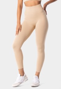 Beige tajice visokog struka napravljene od glatkog, rastezljivog materijala, s oblinama koje prate tijelo i diskretnim logotipom na pojasu.
