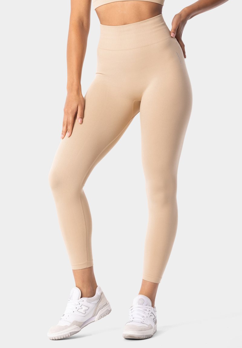 Beige tajice visokog struka napravljene od glatkog, rastezljivog materijala, s oblinama koje prate tijelo i diskretnim logotipom na pojasu.