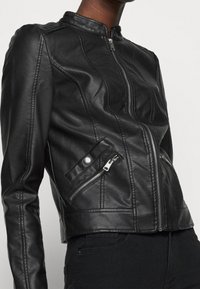 Giubbotto in pelle nera con colletto rialzato, chiusura con zip e due tasche con zip. Presenta dettagli cuciti e un design corto.