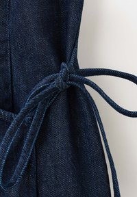 Tissu en denim bleu foncé noué en un joli nœud avec de longues lanières fines sur un fond clair uni.