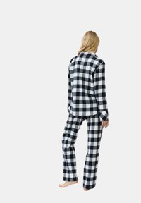Set di pigiama a scacchi bianco e nero, composto da una camicia con maniche lunghe e bottoni e pantaloni coordinati, realizzato in tessuto morbido con una vestibilità rilassata.
