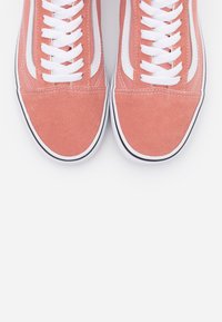 Baskets en daim rose clair avec des lacets blancs, un logo Swoosh blanc et des semelles en caoutchouc noires, présentant un design bas et des coutures soignées.