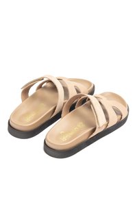 Beige Wildledersandalen mit zwei überkreuzten Riemen und einer gepolsterten Innensohle, ausgestattet mit einer schwarzen Gummisohle und einem goldenen Logo-Detail.