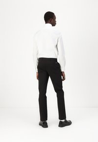 Cămașă albă cu mânecă lungă și pantaloni negri; design ajustat, material neted, fără modele vizibile, asortată cu pantofi negri, privită din spate.
