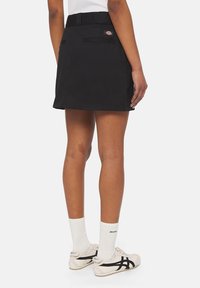 Černá mini sukně s pasem a kapsami. Jednoduchý design, hladká textura a minimální detaily, doplněná bílými ponožkami a teniskami.