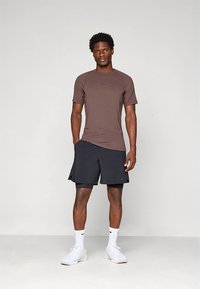 Pruun lühikeste varrukatega spordisärk ja mustad lühikesed püksid. Särgil on väike logo, lühikestel pükstel elastne vöökoht. Valged tossud.