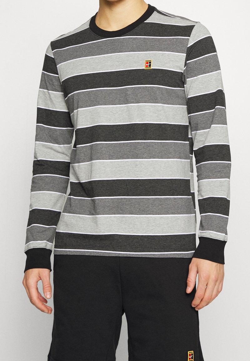 Graues Langarmshirt mit horizontalen schwarzen und hellgrauen Streifen, ausgestattet mit einem runden schwarzen Kragen und einem kleinen gestickten Logo auf der Brust.