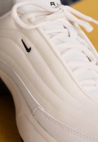 Balti sportiniai bateliai su tekstūruotu tinkleliu, su juodu Nike logotipu, plokščiomis raištelėmis ir aerodinamišku dizainu.