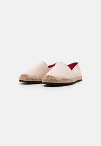 Espadrilles en toile beige avec une semelle en corde de jute, bout arrondi et doublure intérieure rouge. Design simple avec des détails de couture le long des bords.