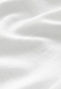 Tessuto bianco con una superficie morbida e leggermente strutturata. Il materiale appare leggero con una caduta fluida e una sottile lucentezza.
