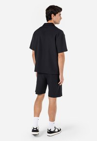 Polo noir à côtes associé à un short noir. La tenue comprend des manches courtes et une coupe décontractée, rehaussée par des baskets noires et des chaussettes blanches.