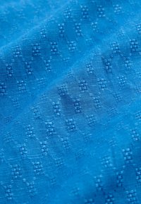 Tissu bleu avec un motif géométrique texturé discret de petits carrés et losanges dans un design tissé.