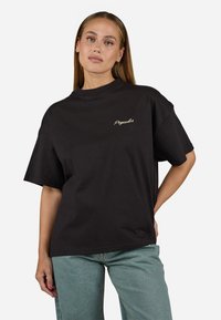 Zwarte oversized t-shirt van katoen, met een ronde hals, korte mouwen en een gouden geborduurd "Pegador" logo op de borst.