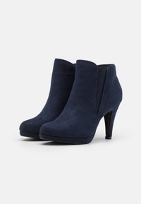 Stivaletti alla caviglia in suede blu navy con un design elegante, punta affusolata, pannelli laterali elasticizzati e un alto tacco a stiletto. Texture liscia e silhouette aderente.