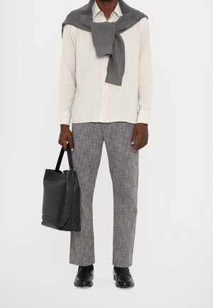 Chemise à rayures claires, pull en tricot gris drapé sur les épaules, pantalon gris texturé, chaussures en cuir noires et sac fourre-tout noir.