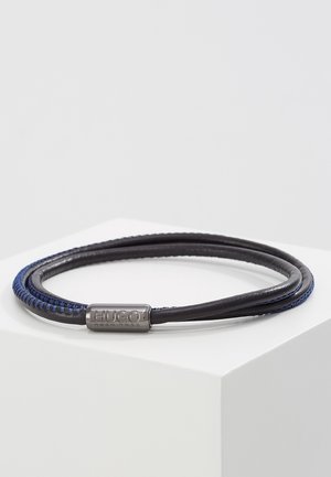 Double black and blue braided leather bracelet with silver magnetic clasp engraved with "HUGO BOSS" displayed on white surface.