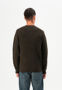 Sweater de malha castanho com um padrão texturizado, gola redonda e mangas longas, combinado com jeans de ganga azuis.