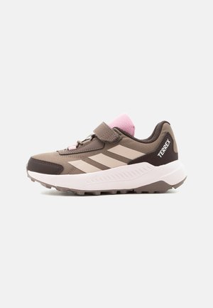 Hnědý a růžový teniska Adidas Terrex s páskem na suchý zip, třemi béžovými pruhy a silnou bílou podrážkou určenou pro venkovní použití.