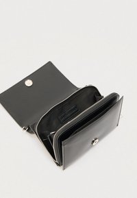 Portafoglio in pelle nera aperto che mostra un scomparto con cerniera e una patta con bottone a pressione su uno sfondo chiaro.