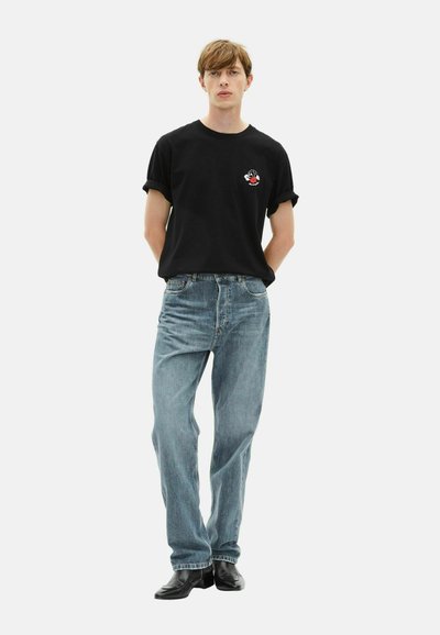 Camiseta de algodón negra con mangas enrolladas y gráfico bordado, combinada con unos jeans de mezclilla azul claro y botas de cuero negras.