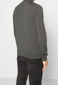 Dunkelgrauer Strickpullover mit hohem Kragen und langen Ärmeln, mit geripptem Saum und Bündchen, kombiniert mit schwarzen Cordhosen.