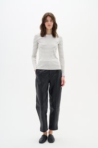 Csíkos hosszúujjú felső fehér és szürke színben, fekete bőrnadrággal párosítva. A modellen fekete slip-on cipők vannak. Minimalista dizájn, testhezálló sziluett.