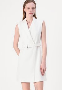 White sleeveless dress with a wrap design, cinched waist belt, and smooth fabric. Features a V-neckline and flat seams for a clean finish.