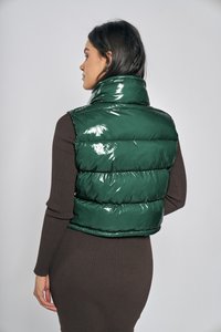 Zielona błyszcząca kamizelka puchowa z wysokim kołnierzem i poziomymi pikowanymi sekcjami, noszona na brązowej, prążkowanej sukience, widziana od tyłu.