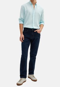 Light blue linen button-up shirt with long sleeves, paired with dark denim jeans and cream sneakers with brown soles.