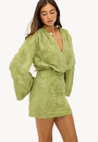 Robe mini texturée avec des franges, vert clair, à manches longues et décolleté en V. Dispose d'une taille cintrée et d'une silhouette fluide.