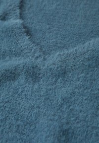 Tessuto azzurro chiaro con una consistenza morbida e pelosa e un bordo leggermente irregolare, che suggerisce un materiale accogliente e caldo.