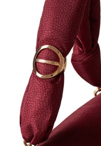 Borsa a tracolla bordeaux con un design in tessuto testurizzato, caratterizzata da un prominente accento in oro rotondo con marchio inciso.