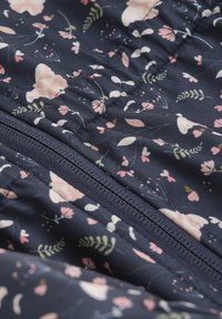 Marint tyg med blommönster i mjuka rosa och gröna nyanser. Inkluderar en synlig dragkedja och vadderad textur.