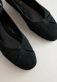 Fekete bőrhatású balerina cipő lekerekített orral, elöl keresztbe átfedő mintával és sima fekete belsővel. Puha textúra, minimális mintázati részletekkel.